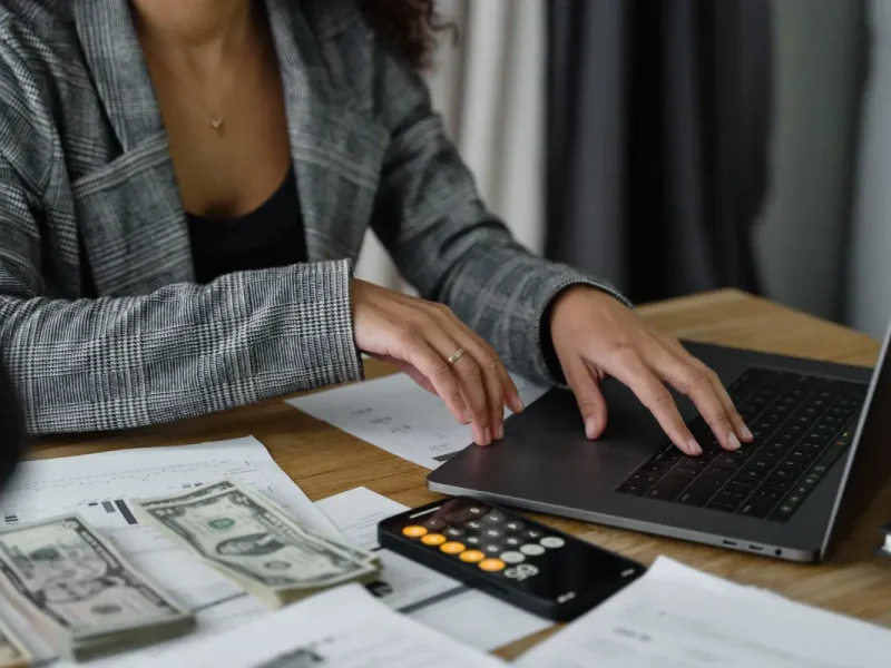 Vrouw berekent met een calculator en laptop.