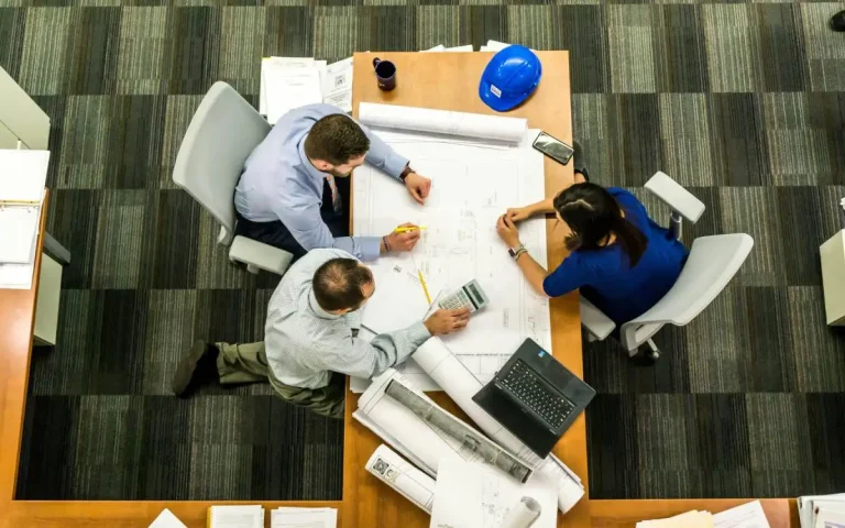 Drie werknemers vergaderen en zitten naast een bureautafel.