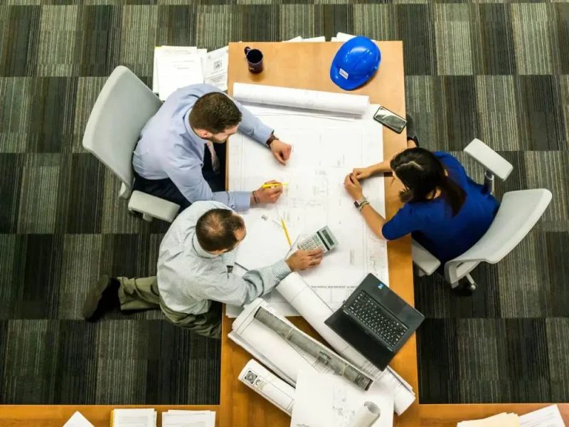 Drie werknemers vergaderen en zitten naast een bureautafel.