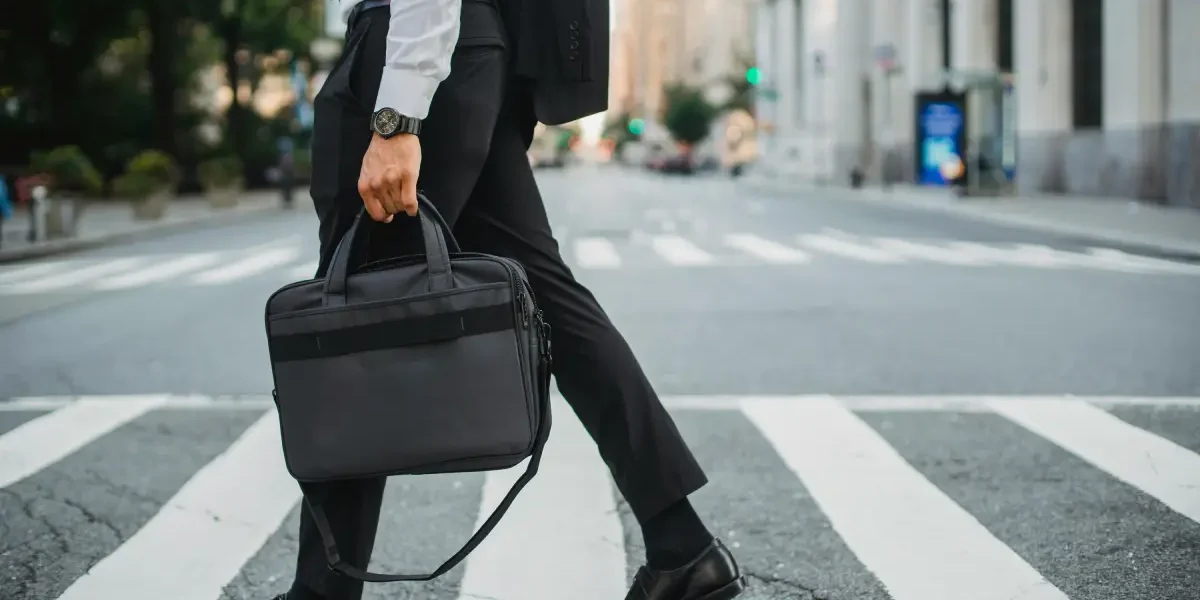 Een zakenman loopt over een zebrapad op straat en heeft een laptoptas in zijn hand.