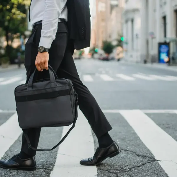 Een zakenman loopt over een zebrapad op straat en heeft een laptoptas in zijn hand.