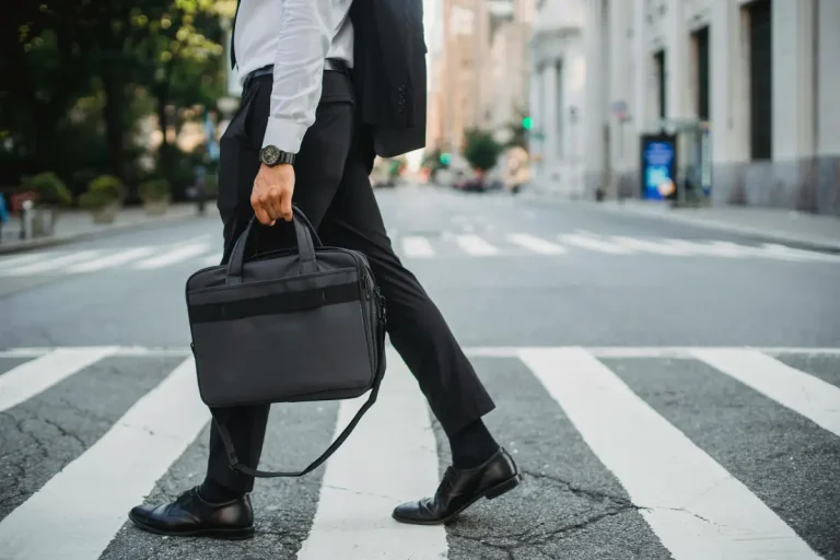Een zakenman loopt over een zebrapad op straat en heeft een laptoptas in zijn hand.