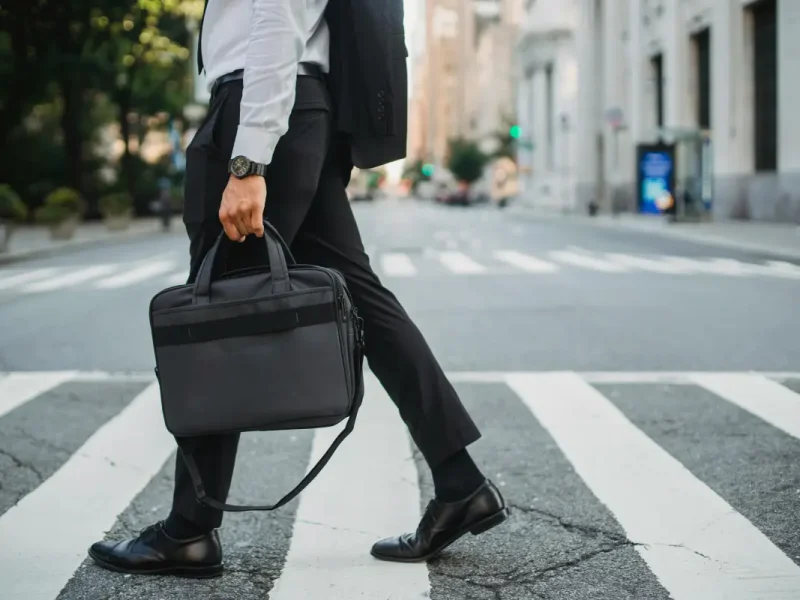 Een zakenman loopt over een zebrapad op straat en heeft een laptoptas in zijn hand.