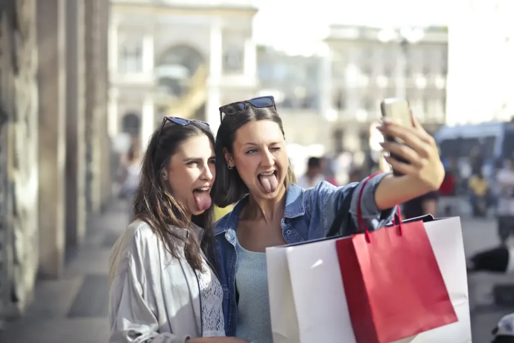 Twee vrouwen maken een selfie met hun tong uitgestoken met shop tassen.