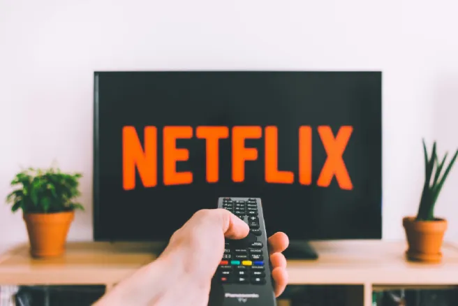 Een tv met Netflix erop en een persoon met een afstandsbediening in de hand